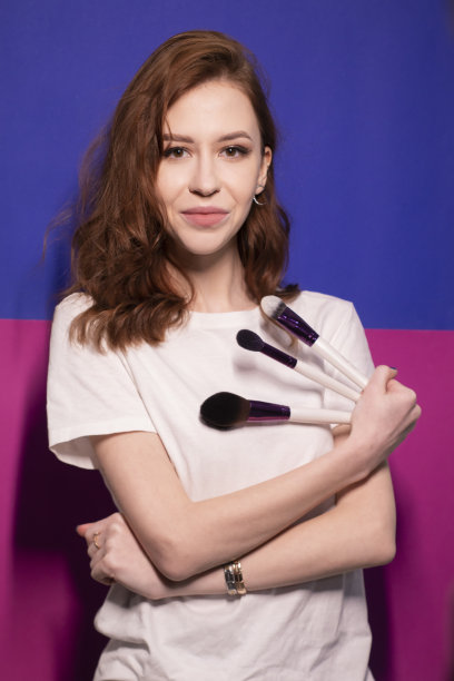 迷人的黑发女子在白色t恤与化妆刷隔离在彩色的蓝色和粉红色的背景。专业化妆师图片下载