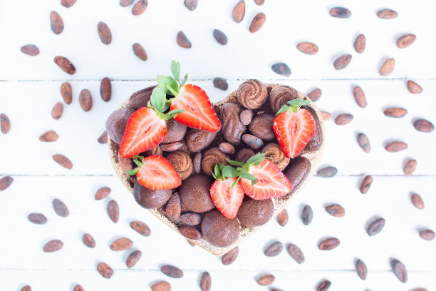 这是一个情人节心形的盒子，里面有巧克力和新鲜的草莓，可可豆，可可在白色的木质背景上。平的。情人节，爱，礼物。图片下载