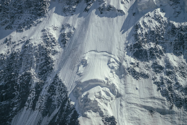 大岩石雪山墙的自然背景与白色冰川和雪檐口近距离。阳光下的雪山边，美丽的自然纹理。黑白色的高山的完整框架。图片下载