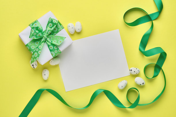 复活节春节贺卡与礼品盒与绿色丝带，鸡蛋和甜胡萝卜在粉红色的背景与地方文字。前视图。图片下载