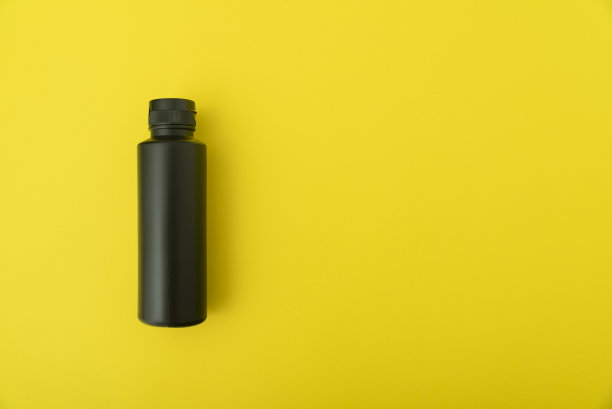 黄色背景下的黑色小瓶。副本的空间。模拟。图片下载