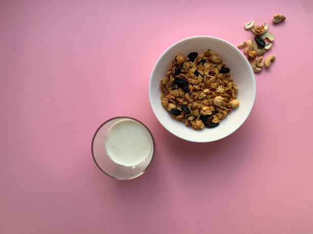 白色碗里有自制的格兰诺拉麦片和酸奶，背景是柔和的粉红色。照片与顶视图。适当的营养，健康的早餐。图片下载