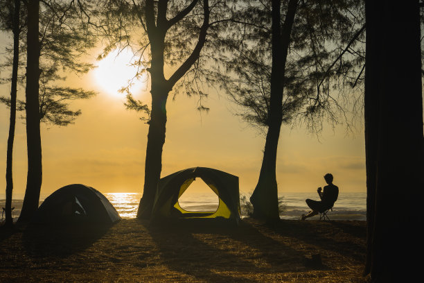 剪影露营帐篷和人们放松在海滩上日出和大海的背景图片下载