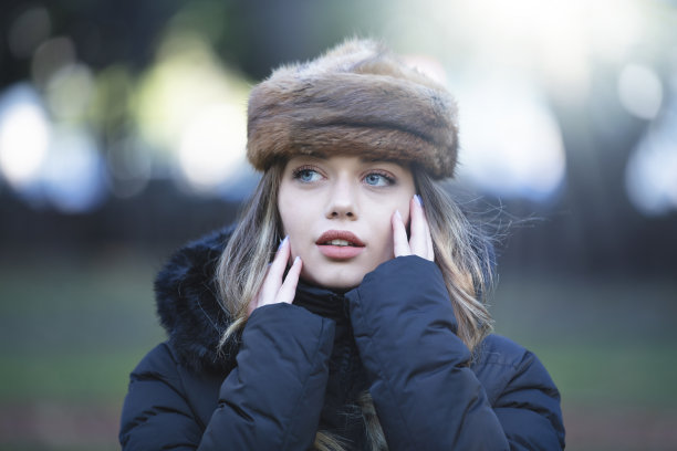 美丽的金发年轻女子肖像在模糊的背景，她戴着一顶毛皮帽子图片下载