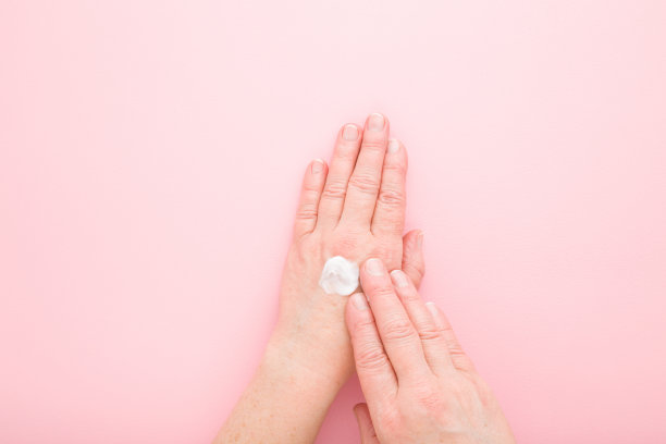 老年成熟女性双手使用抗老化保湿白色霜在浅粉色的桌子背景上。柔和的颜色。关心清洁和柔软的身体皮肤。每天的美容产品。特写镜头。自顶向下的观点。图片下载