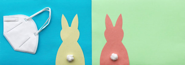 FFP2保护面具和两个纸复活节兔子在绿色和蓝色的背景。图片下载