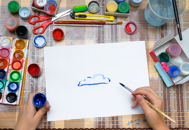 一个女孩在一张空白的白纸上画着水彩蓝云，在家里进行艺术创作，创作艺术作品图片下载