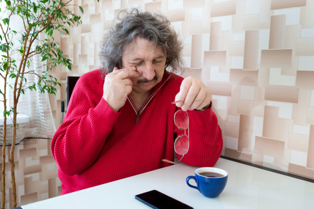 一位老人在长时间使用手机后，摘掉眼镜，疲惫地用手揉搓眼睛。眼睛疼。图片下载
