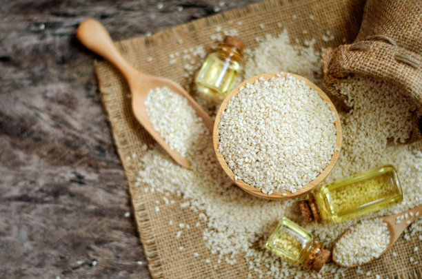 俯视图干燥的有机白芝麻种子在木碗上模糊的背景一些在麻袋织物和垃圾地板上与香油在玻璃瓶，在深棕色调图片下载