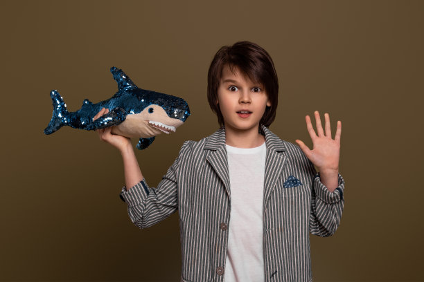 一个小男孩的肖像，在他的手在工作室的一个玩具鲨鱼在绿色的背景。随意的风格图片下载