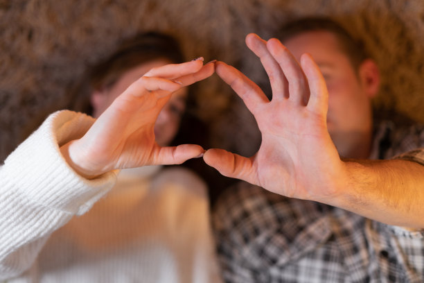 一对夫妇，一男一女，躺在地板上，用手指做一个心形。情人节和家人。图片下载