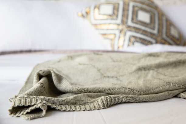 舒适的床，柔软的枕头，床单，针织毯。装饰材料阁楼桌子，时钟，小植物和美丽的设计灯。图片下载