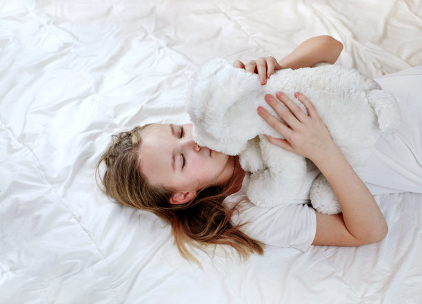 小女孩抱着她的玩具在床上，享受甜蜜的梦图片下载