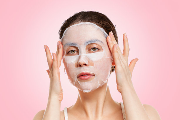 一个年轻美丽的白人妇女的肖像平滑布面具与她的手指。粉红色的背景。美丽、水合、自我护理的理念图片下载