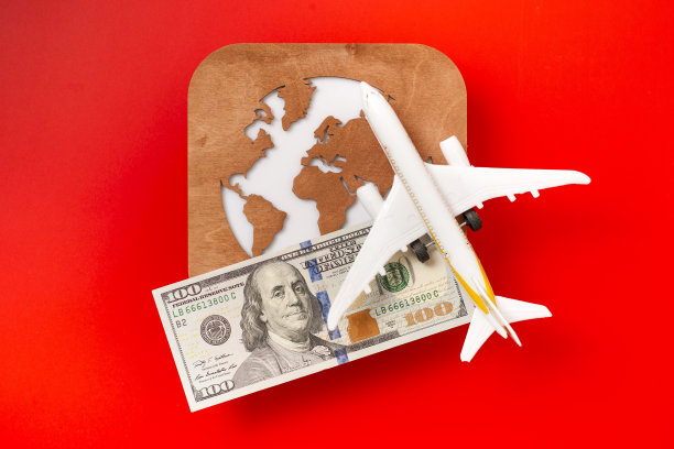 一个地球仪，一架玩具飞机和一张红色背景的100美元钞票。旅游的概念图片下载