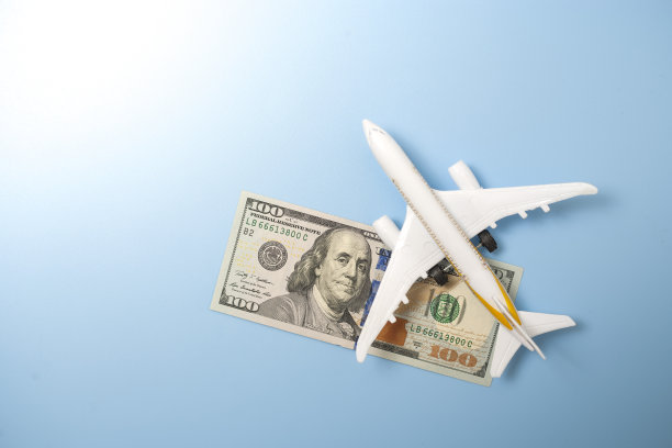 一个地球仪，一架玩具飞机和一张有蓝色背景的100美元钞票。旅游的概念图片下载
