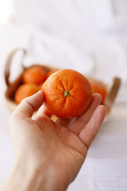 一个年轻女人手里拿着橘子，后面放着一篮子橘子图片下载