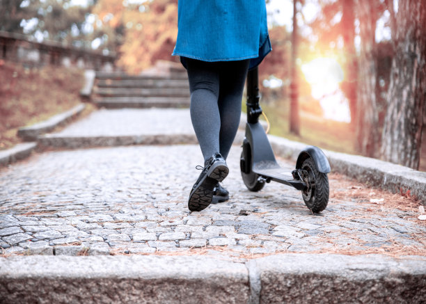女性的腿在鹅卵石街道上电动踏板车图片下载