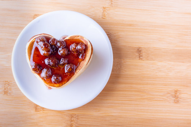创造性的早餐。木制背景的白色盘子上自制的带有浆果果酱的心型煎饼图片下载