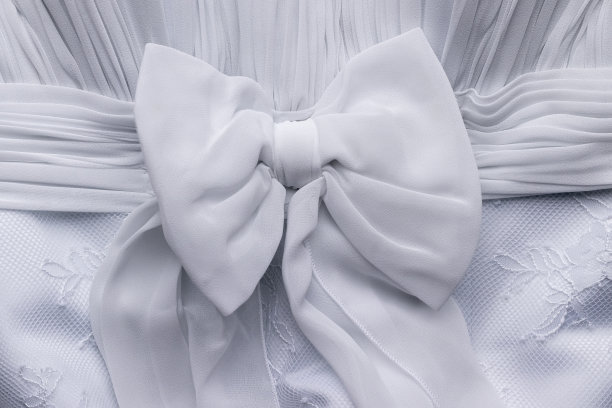 精致的白色蝴蝶结上的婚纱特写。纺织面料装饰背景图片下载