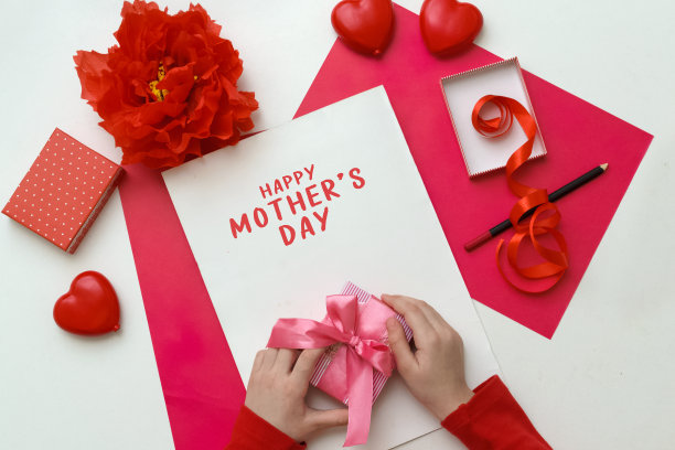 金发小女孩制作母亲节或生日贺卡，手里拿着礼物放在白色的桌子上。图片下载