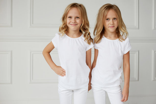 两个穿着白色衣服的小女孩被孤立在白色背景上。双胞胎女孩手牵着手。图片下载