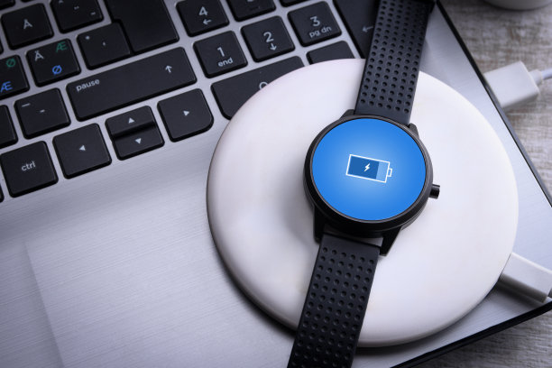 智能手表无线充电与屏幕上的充电指示。在台式机旁边，在笔记本电脑旁边。前视图。图片下载