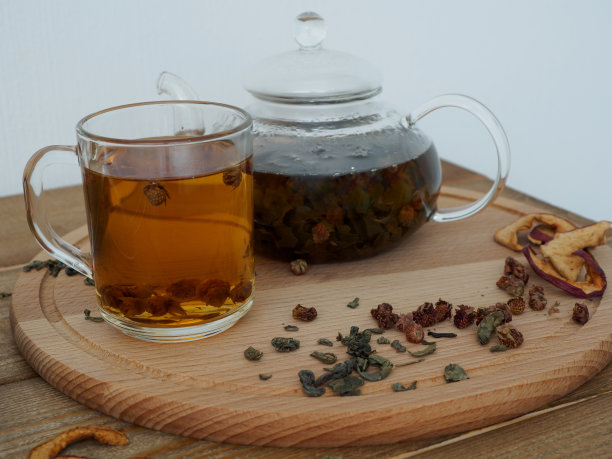 热的黑色凉茶放在一个木制托盘上的茶壶里，一杯茶在白色的背景上。健康浆果和水果干图片下载