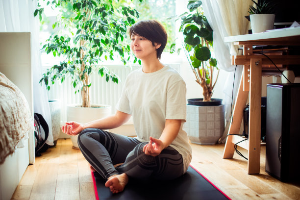 一个女人坐在她床前的垫子上，在卧室里做瑜伽姿势。在家练习放松瑜伽。健康的生活方式。家在线训练。软选择聚焦图片下载