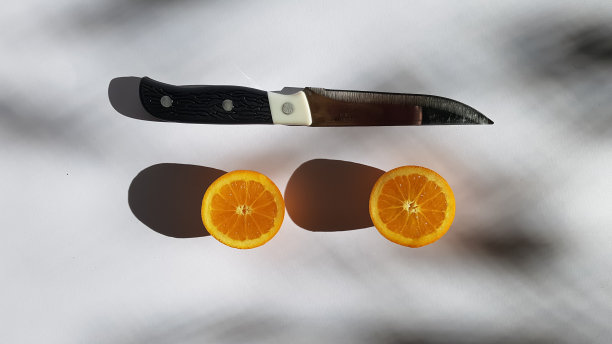 在柔和的阳光下，一个橙子从中间切开，用刀放在白色的表面上图片下载