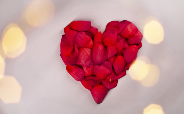 粉红色背景上的红玫瑰花瓣的心。图片下载