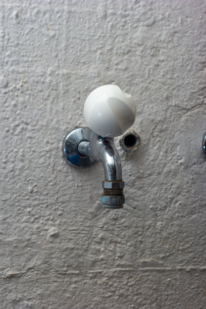 在洗衣房墙上安装的老式水龙头，带有白色圆形旋钮图片下载