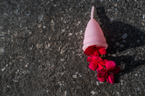 硅胶月经杯，灰色背景，花瓣象征女性月经期。可重复使用的环保女性卫生用品。零浪费、可持续、无塑料的生活方式图片下载