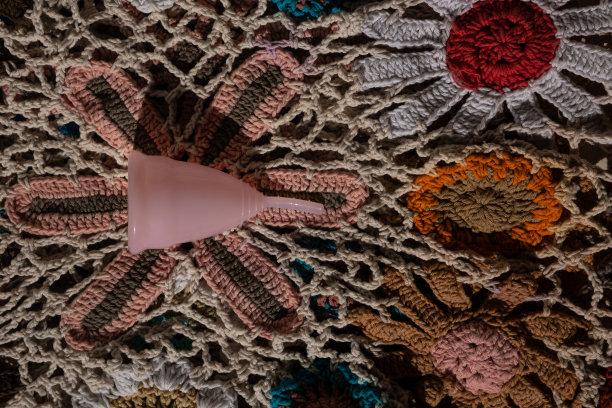 粉红色硅胶月经杯上彩色针织背景。可重复使用的环保女性卫生用品。零浪费、可持续、无塑料的生活方式图片下载