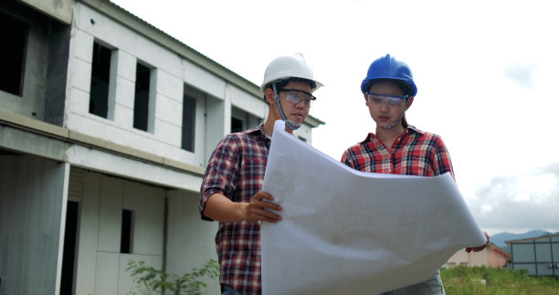 年轻亚洲男女工业工程师在建筑工地安全设备。与其他工人定额规划施工现场，佩戴蓝、白安全帽。图片下载