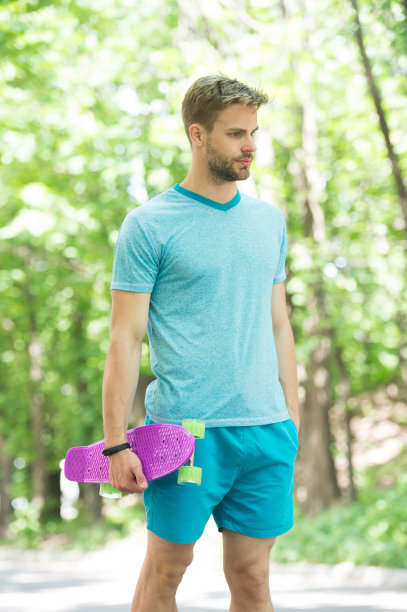 只要试着骑一次，你就会爱上它。他拿着硬币板准备骑。男子严肃的脸扛便士板公园自然背景散焦。男人喜欢滑板和运动的生活方式图片下载