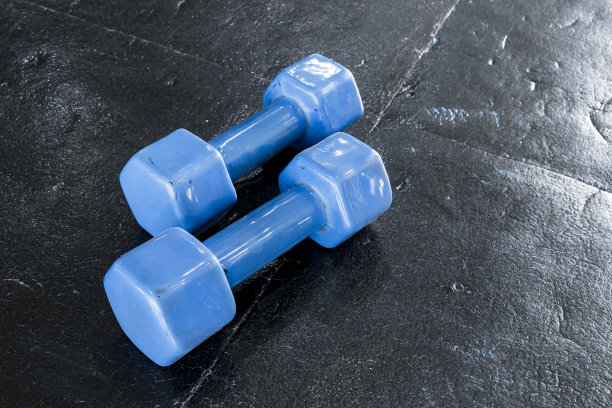 一对蓝色硬塑料六角形哑铃躺在体育馆或健身俱乐部的橡胶垫子上。图片下载