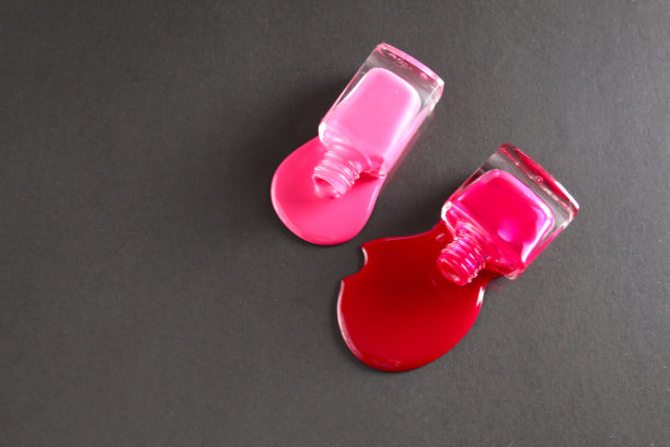 美丽的背景两瓶指甲油瓶子红色或紫红色的粉红色溢出倒在桌子上的一个黑色的背景近景从侧面从顶部与copyspace图片下载