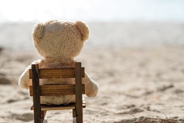 泰迪熊坐在带海景的木椅上。爱和关系的概念。美丽的白色沙滩在夏天。图片下载