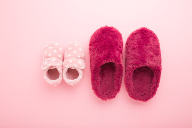 美丽柔软温暖的母亲和婴儿女孩拖鞋在浅粉色的桌子背景。柔和的颜色。特写镜头。舒适的鞋。自顶向下的观点。图片下载