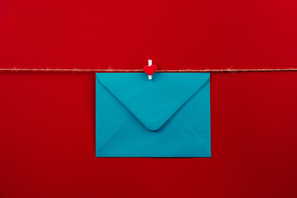 一个封闭的蓝色信封与衣夹与一颗心挂在绳子孤立的红色背景。给朋友写封信。邮政信封。明信片的礼品信封。情人节快乐，14号图片下载