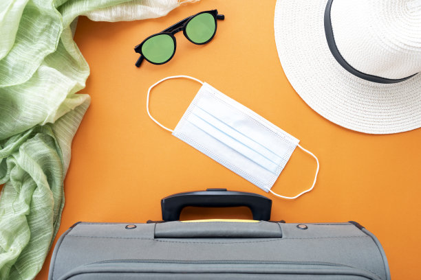 平躺在复印空间，一个行李箱，口罩，太阳帽，太阳镜和一条围巾被安排在一个橙色的背景。2019冠状病毒病大流行期间的旅行概念。图片下载