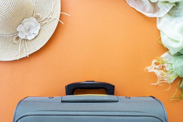 平躺在复印空间，一个行李箱，一顶太阳帽和一条围巾被安排在一个橙色的背景。旅行概念与文本复制空间。图片下载