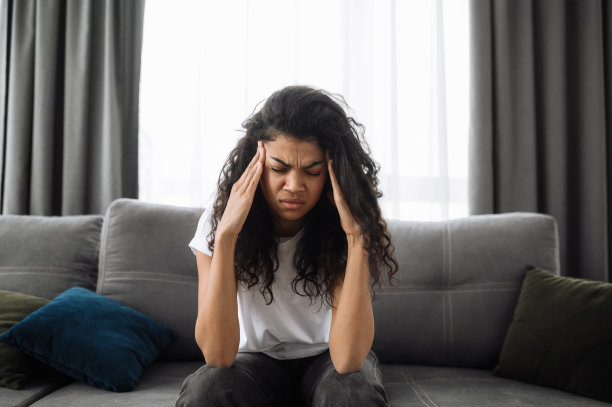 一张悲伤的非洲裔美国年轻女子的照片。褐发女人在家里无聊，疲惫或压力。心烦意乱的女孩坐在沙发上，头痛或感到沮丧图片下载