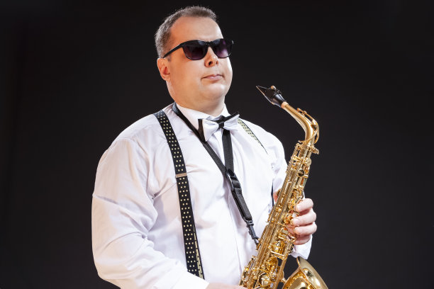 成熟的白种人萨克斯管吹奏者在白色衬衫在太阳眼镜在无缝的黑色背景。水平Compostiion图片下载
