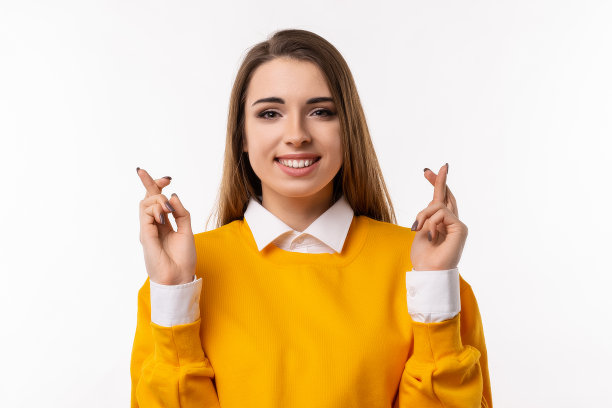 迷人的黑发女孩交叉手指好运，祈祷愿望成真。工作室拍摄白色背景图片下载