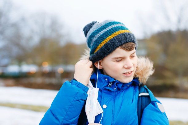 一个戴着医用口罩的小男孩在去学校的路上。孩子背包背包。学生在寒冷的秋冬天穿上暖和的衣服。冠状病毒大流行期间的封锁和隔离时间图片下载