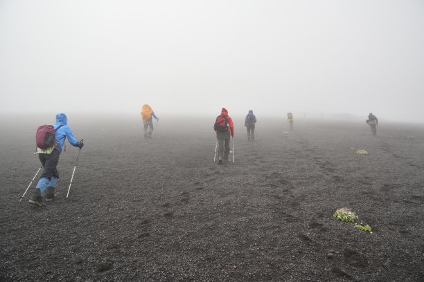 游客们背着背包，拿着杆子，爬上一座覆盖着碎石的迷雾山的斜坡。图片下载