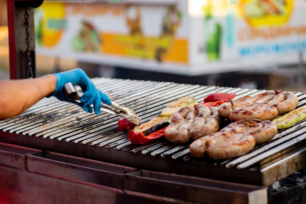 厨师把烤好的香肠和蔬菜翻过来。街头食品。烧烤野餐图片下载