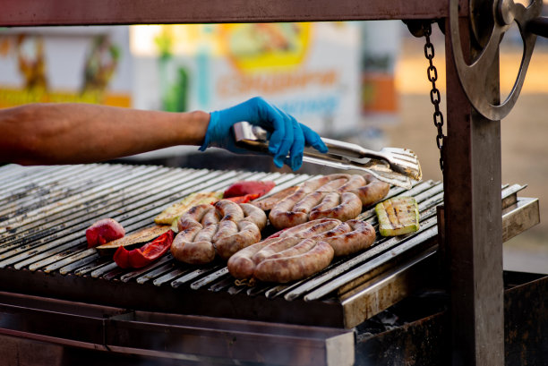 厨师把烤好的香肠和蔬菜翻过来。街头食品。烧烤野餐图片下载